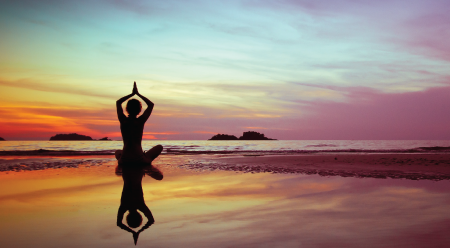 person meditating on a beach during a sunset